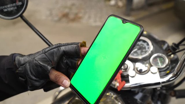 Hand shot of a rider using green screen smart phone on his motor bike. Close up of chroma  key smart phone.