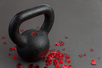 Holiday fitness, black kettlebell, with red heart confetti, on a black gym floor