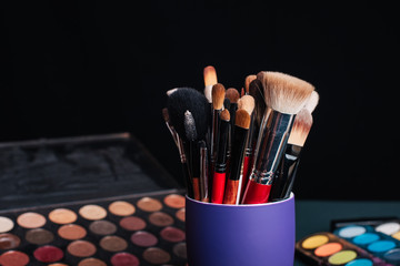 set of professional makeup brushes on a palette background with colored eye shadows