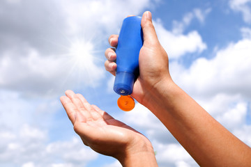 Hand of female holding sunscreen. Very sun light Sky background.Health concepts and skin care