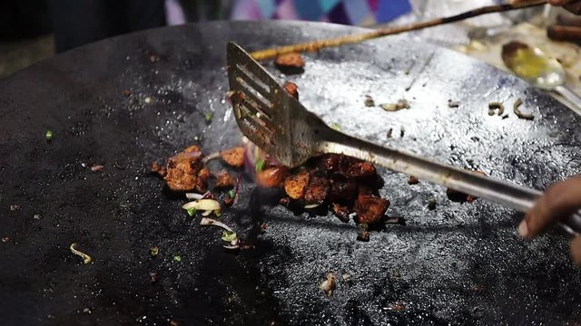 small pieces of chicken being fried on a big frying pan with onion for preparation of kathi kebab roll