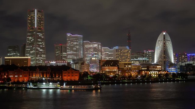 Timelapse Yokohama city quay illuminated at night with popular Ferris wheel changing colors by highrise tower and skyscrapers