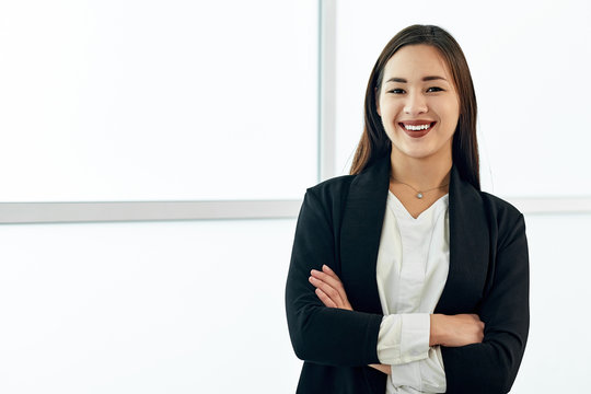 Smiling asian business woman in modern office on white background. crossed arms.
