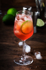 Campari tonic alcohol cocktail with red bitter, tonic, lime and ice. Old wooden table background, bar tools, selective focus. Copy space