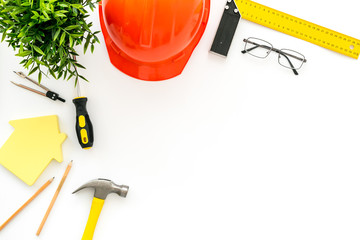 Construction concept. Helmet, tools on work desk, house cutout on white background top-down frame...