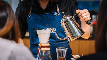 Women Barista to make a drip brewing, filtered coffee, or pour-over is a method which involves pouring water over roasted, ground coffee beans contained in a filter. in a coffee shop.vintage tone.