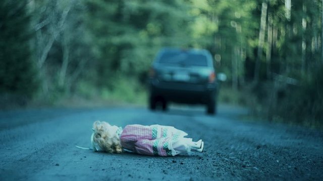 Creepy and eerie shot of car driving off leaving doll behind on ground