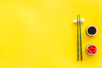 Set of chopsticks for sushi, ginger and soy sause on yellow background top-down frame copy space