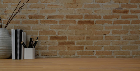 close up view of vintage workspace with office supplies and vase on wooden table with brick wall