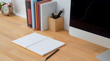 Close up view of modern workspace with note book, computer and office supplies on wooden table background