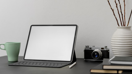 Close up view of blank screen tablet  with coffee cup, stylus, camera and decoration on black desk with white wall