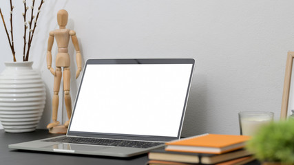Close up view of modern workspace with mock up laptop, wooden figure, books and decorations on black desk with white wall