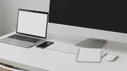 Cropped shot of workspace with blank screen laptop, computer, smartphone and notebook on white table