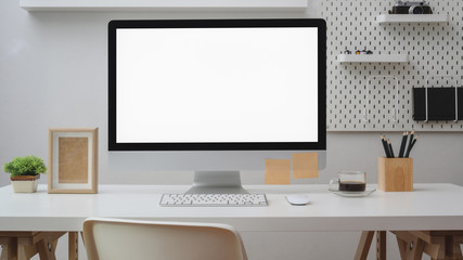 Close up view of  workspace with blank screen computer, office supplies, decoration and shelf on white desk with white wall