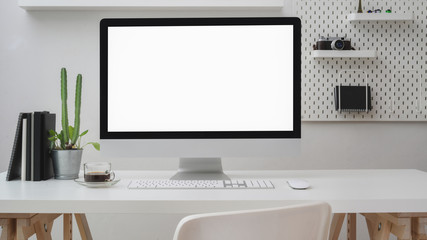 Close up view of workspace with blank screen computer, office supplies, decoration and shelf on white desk with white wall