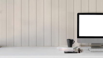 Close up view of workspace with blank screen computer, smartphone, coffee cup and office supplies on white table with plank wall