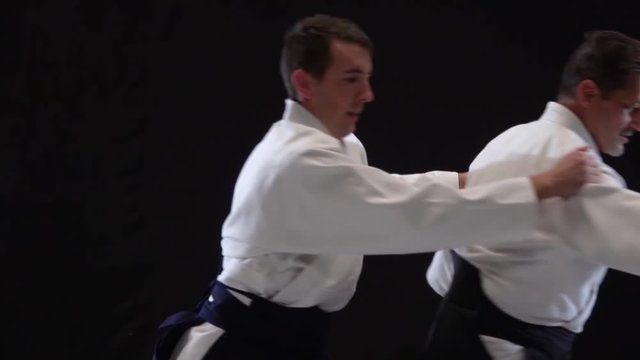 Two Masters participants of the training in special clothes of aikido hakama work out the methods of single combat on spotlights background. Slow motion. Close up.