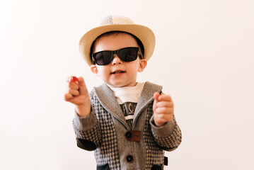 Happy baby boy in grey suit, hat and glasses on light background