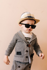 Happy baby boy in grey suit, hat and glasses on light background