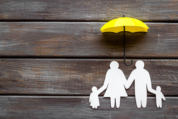 Live insurance concept. Family silhouette protected by umbrella on dark wooden background top-down...