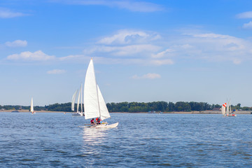 A yacht with a white sail floats on the river as part of a sailing regatta