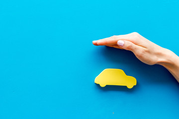 Car insurance. Hand defends automobile cutout on blue background top-down copy space