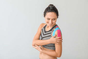 Sporty woman with physio tape applied on shoulder against light background