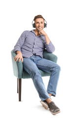 Handsome man listening to music while sitting in armchair on white background