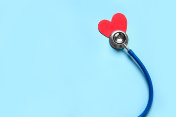 Modern stethoscope and red heart on color background