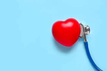 Modern stethoscope and red heart on color background