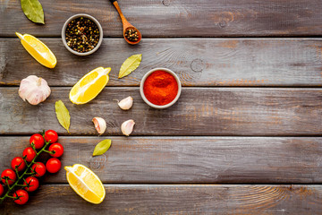 Cooking background with spices - pepper, garlic, cherry tomatoes - on dark wooden desk top-down frame copy space