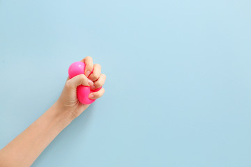 Female hand squeezing stress ball on color background - obrazy, fototapety, plakaty