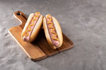 Hot dogs with mustard on a wooden board. Hot dogs served on a stone table. Free space for text
