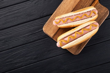 Hot dogs with mustard on a wooden board. Hot dogs served on a black table. Free space for text