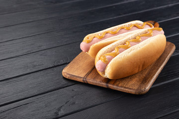 Hot dogs with mustard on a wooden board. Hot dogs served on a black table. Free space for text