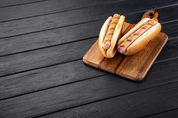 Hot dogs with mustard on a wooden board. Hot dogs served on a black table. Free space for text