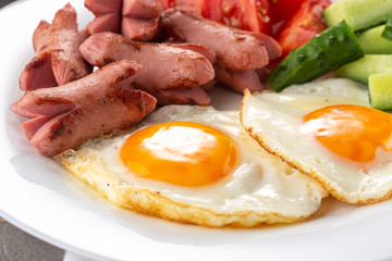 Homemade delicious breakfast with sunny side up fried egg, sausage, vegetable, jam, black coffee on a stone table. Breakfast served with flowers and white dishes