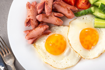 Homemade delicious breakfast with sunny side up fried egg, sausage, vegetable, jam, black coffee on a stone table. Breakfast served with flowers and white dishes