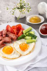Homemade delicious breakfast with sunny side up fried egg, sausage, vegetable, jam, black coffee on a stone table. Breakfast served with flowers and white dishes