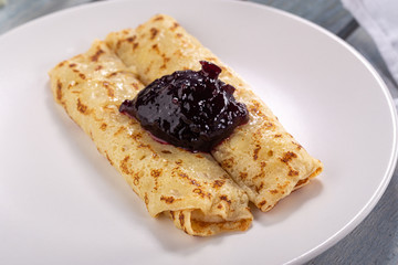 Homemade pancakes with cream cheese and berry jam on a plate, selective focus. Wooden table