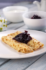 Homemade pancakes with cream cheese and berry jam on a plate, selective focus. Wooden table