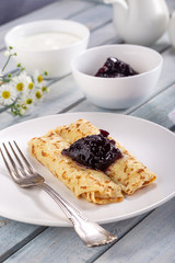 Homemade pancakes with cream cheese and berry jam on a plate, selective focus. Wooden table