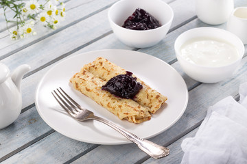 Homemade pancakes with cream cheese and berry jam on a plate, selective focus. Wooden table