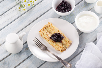 Homemade pancakes with cream cheese and berry jam on a plate, selective focus. Wooden table