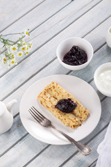 Homemade pancakes with cream cheese and berry jam on a plate, selective focus. Wooden table