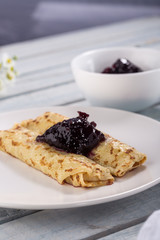 Homemade pancakes with cream cheese and berry jam on a plate, selective focus. Wooden table