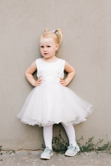 Happy baby girl in white dress on grey background