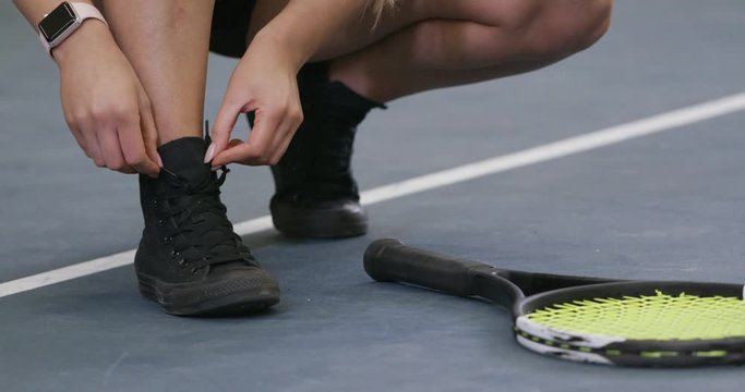 Young female tennis player tying shoelaces on sports shoes, training day.