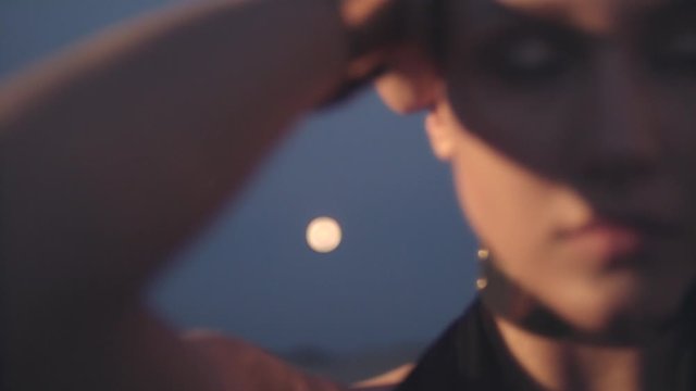 Portrait of young woman at night in the desert dancing in front of the full moon.