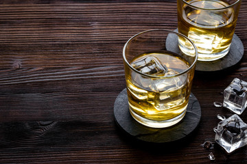 Whiskey near ice cubes on dark wooden background copy space